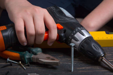 Work with power tools. The hand holds a screwdriver. screw, pliers and screwdriver on a wooden table