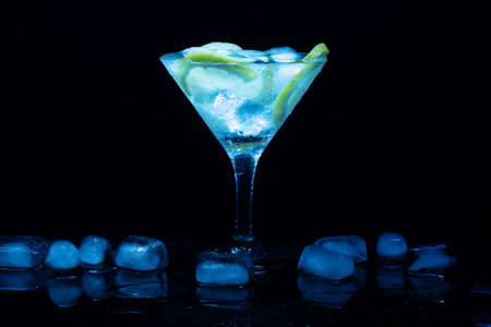 Cocktail martini with ice and lime in a glass on black tableの写真素材