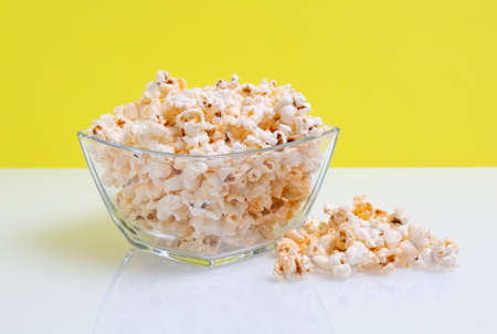 popcorn in a glass bowl on yellow backgroundの写真素材