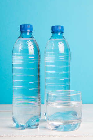 Plastic bottle of healthy water and glass with water on blue backgroundの写真素材