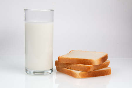 Glass with milk and bread on white table. Natural healthy wholesome breakfastの写真素材