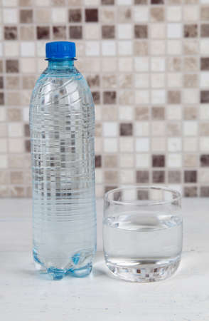 Glass of water and plastic water bottle on kitchen tableの写真素材