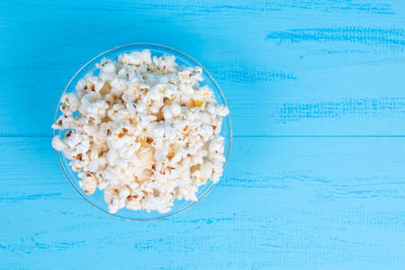 white salty popcorn in a glass bowl on a blue table. Top view with copy spaceの写真素材