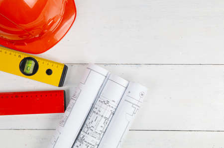 Safety helmet, paper drawings, blueprits and building level on a white table. The work of a civil engineer. Top view vith copy spaceの写真素材