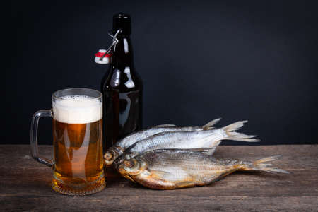 Glass of beer, dry fish and beer bottle on a black background