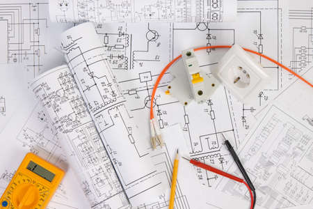 Paper electrical engineering drawings with circuit breaker and multimeter.
