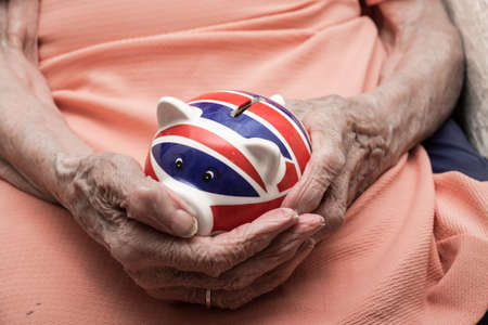 Pensioner hands holding piggy bank with british flag design