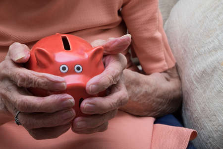 Old hands of pensioner holding piggy bank, saving for care home or death duties, inheritance taxの写真素材