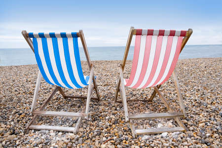 Deckchairs on beach, typical english seaside holiday scene, red and blue stripes representing main political party of labour or conservativeの写真素材