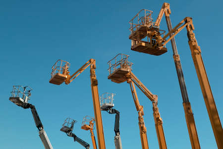 Cherry pickers in a row against blue skyの写真素材