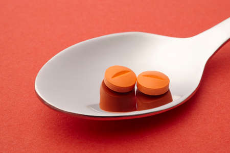 Pill and spoon detail. Orange background. Medicament treatment. Health care photoの写真素材