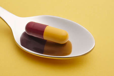 Pill and spoon detail. Yellow background. Medicament treatment. Health care photoの写真素材