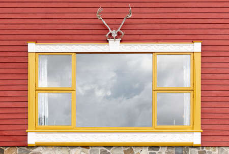 Red wooden facade with yellow window and deer horn. Horizontalの写真素材