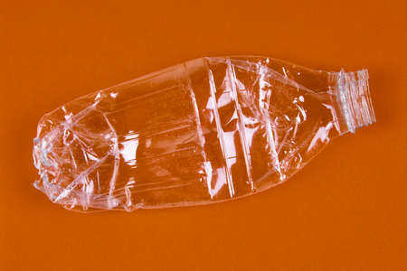 Crushed plastic bottle with brown background. Recycled garbage. Horizontal