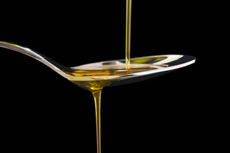 Olive oil liquid on a spoon over black background. Cookingの写真素材