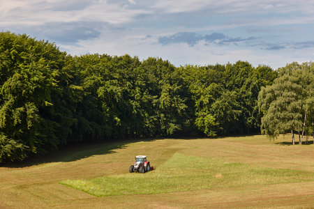 Tractor mowing grass. Meadow sorrounded by forest. Agriculture landscapeの写真素材