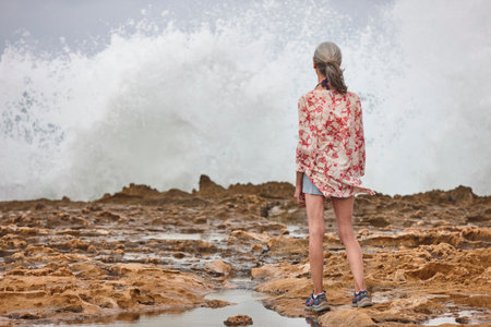 Senior woman looking the sea. Waves breaking on the shore