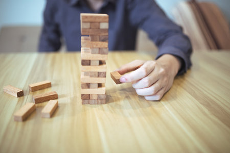 Business strategy concept with hands playing a wooden block tower game, symbolizing risk and...