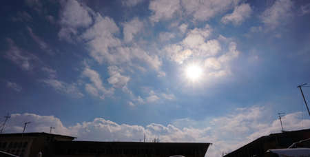 The sun is visible between the blue sky and the white cloudsの写真素材