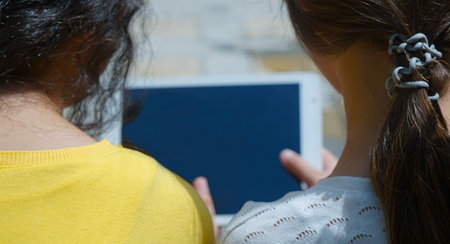 Two girls sitting in front of the window are watching the tabletの写真素材