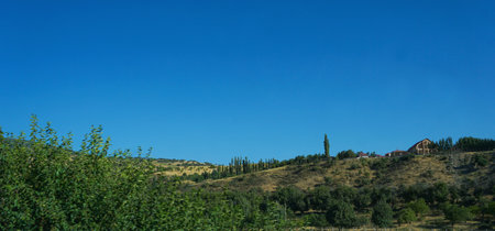 A blue sky and a house can be seen on top of the mountain
