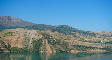 At the foot of the mountain, near the lake, there are hills and housesの写真素材