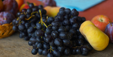 Black grapes and various fruits are scattered on the board in front of the windowの写真素材