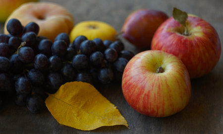 On the board are black grapes, yellow leaves, and various fruitsの写真素材