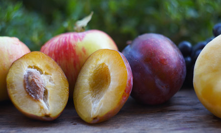 Plums cut in half and there are other fruits behind themの写真素材