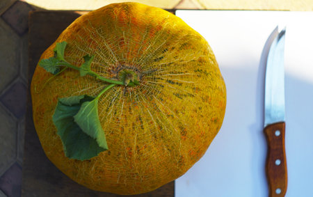 round yellow melon and knife on a board