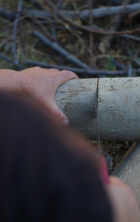 In the yard, a man is sawing a log with a hand saw.