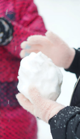 The girl is rolling snow in her hands. Winter season