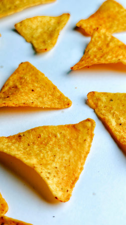 Crispy golden triangle corn chips close up on a clean white background showcasing crunchy texture, savory seasoning, and delicious snack detail perfect for food branding, advertisiの写真素材