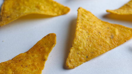 Crispy golden triangle corn chips close up on a clean white background showcasing crunchy texture, savory seasoning, and delicious snack detail.の写真素材