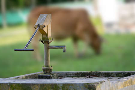 Old hand-operated water pump standing on roadside in theの写真素材