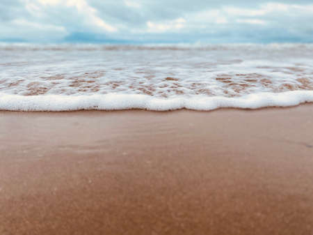 A wave gently rolling over wet sand of a beach on a tranquil summer day.の写真素材