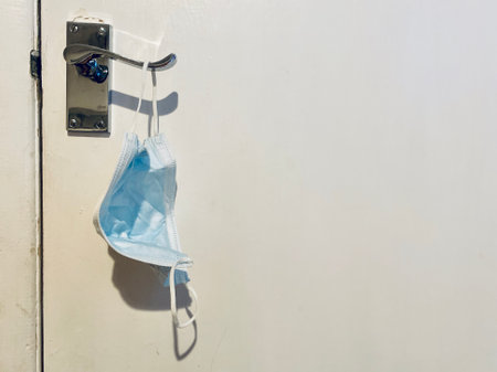Three layer blue and white medical face mask hanging on a chrome door handle.の写真素材