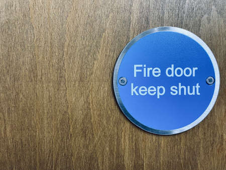 Fire door keep shut sign on stained oak door, with space for text.