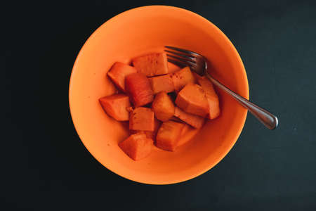fresh orange papaya in a bowl with a fork photographed with a black backの写真素材