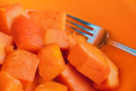 fresh orange papaya in a bowl with a fork photographed with a black backの写真素材