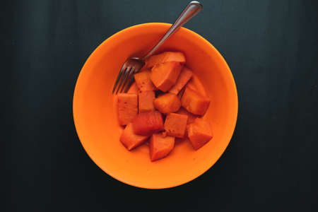 fresh orange papaya in a bowl with a fork photographed with a black backの写真素材