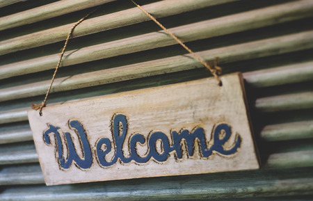 Rustic wood welcome sign hanging by rope on antique door. Greeting signboard.の写真素材