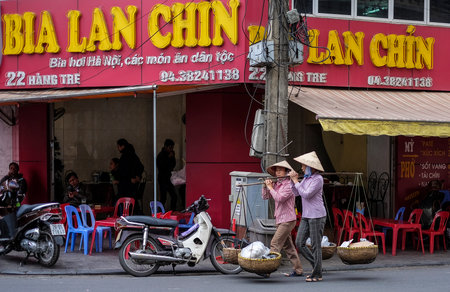 HANOI, VIETNAM - DECEMBER 11, 2014 : Vietnamese street market lady seller. They carrying a Òquang ganhÓ (two baskets slung from each end of a wooden or bamboo pole) filled up with food.のeditorial素材