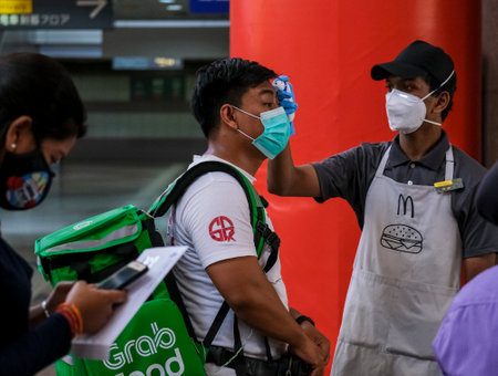 KUALA LUMPUR, MALAYSIA - MARCH 22, 2020: People wearing a face mask and check the body temperature to prevent infection of the virus. Coronavirus disease 2019 (COVID-19) outbreak.のeditorial素材
