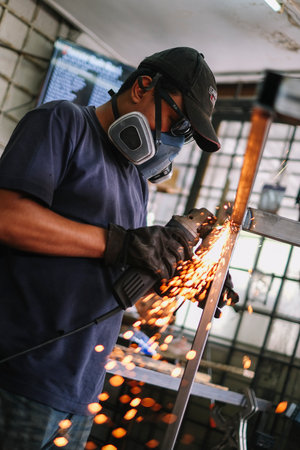 KUALA LUMPUR, MALAYSIA - MARCH 23, 2021: Worker wearing protection mask grinding welded metal and...
