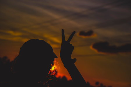 Female showing peace sign on nature bokeh blur sunset background. Copy space with the concept of happy love valentine's dream travel and freedom.の写真素材
