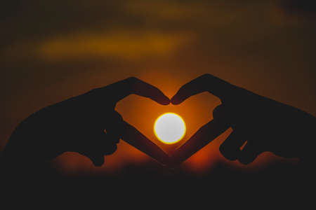 Female hands heart shape by fingers on nature bokeh blur sunset background. Copy space with the concept of happy love valentine's dream travel and freedom.の写真素材