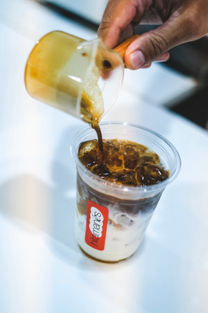 KUALA LUMPUR, MALAYSIA - MARCH 01, 2022: Professional Barista poured a espresso into iced milk for...