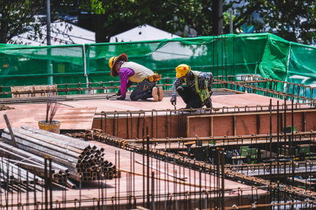 KUALA LUMPUR, MALAYSIA - MARCH 28, 2023: Construction workers wearing safety protective equipment while working on high-rise buildings at the construction site. Economy and development.のeditorial素材