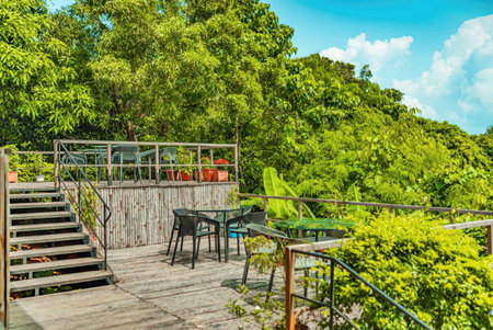 Wooden deck with green chairs and table surrounded by lush tropical greenery